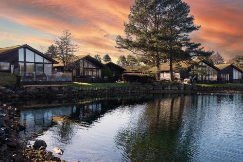 a house with a lake in front of a sunset at Sandmartin Lodge a lakeshore haven Pine Lake Resort in Carnforth