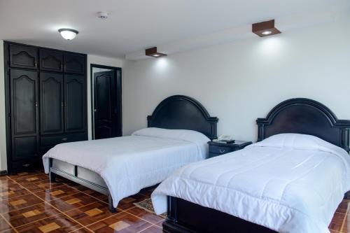 two beds in a bedroom with black cabinets and white sheets at Hostería El Prado in Ibarra