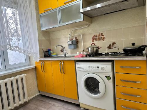 a kitchen with a washing machine and yellow cabinets at Luxe-apartments 2х in Taraz