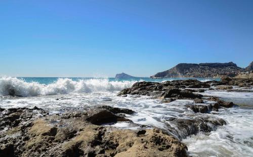 a beach with waves crashing on the rocks at Residencial Terra de Mar Calpe, Grupo Terra de Mar, alojamientos con encanto in Calpe