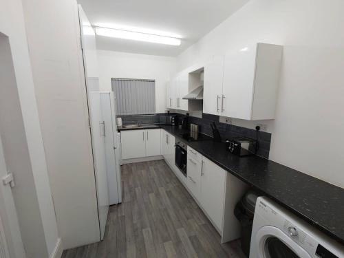 Una cocina con gabinetes blancos y una encimera negra. en C Spacious 5 Bed - Pkg WiFi Long Stays, en Norton Canes
