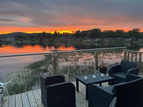 a sunset over a lake with two chairs and a table at Gressingham 9 - South Lakes Leisure Village - lodge on the lake in Carnforth