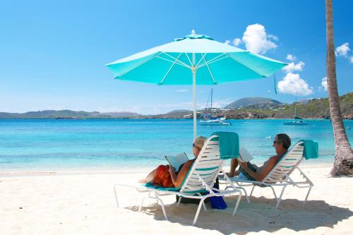 two people sitting in chairs under an umbrella on the beach at Secret Harbour Beach Resort in St Thomas