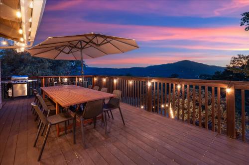 a wooden deck with a table and chairs and an umbrella at Yosemite Lookout Lodge w/ hot tub, firepits, game room, and more in Oakhurst
