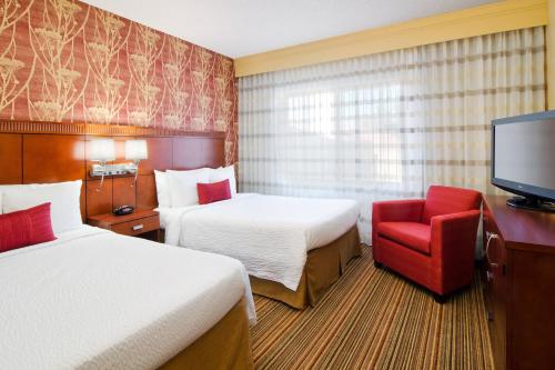 a hotel room with two beds and a red chair at Courtyard by Marriott Albuquerque Airport in Albuquerque