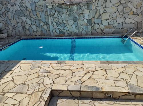 a swimming pool with a stone wall and blue water at Chácara das Oliveiras in Campinas