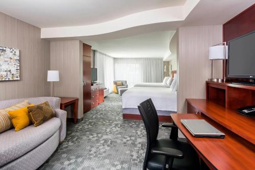 a hotel room with a couch and a bed and a television at Courtyard by Marriott Kalamazoo Portage in Portage