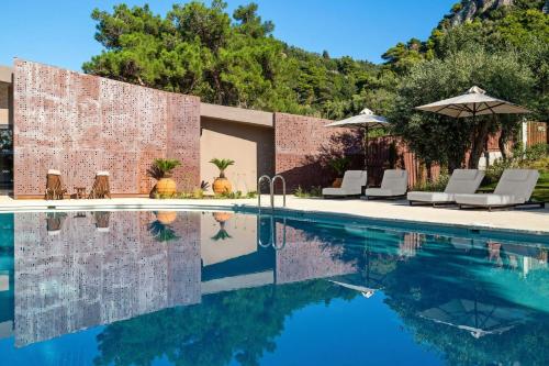 a pool with chairs and umbrellas next to a brick wall at Domes of Corfu, Autograph Collection in Glyfada