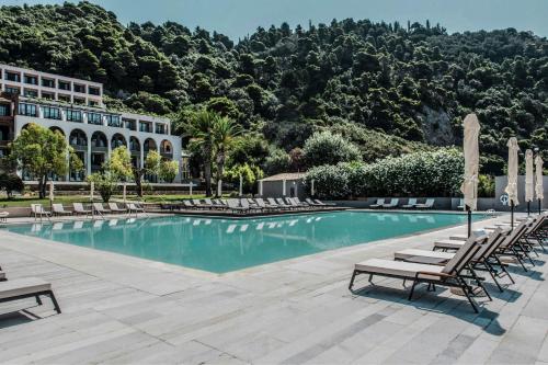 a swimming pool with lounge chairs and a building at Domes of Corfu, Autograph Collection in Glyfada