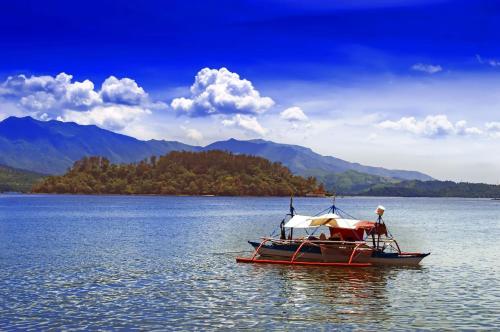 a boat on a lake with mountains in the background at RedDoorz @ CMS Apartelle Olongapo City in Olongapo