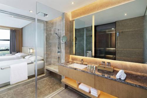 a bathroom with a sink and a shower and a bed at Courtyard by Marriott Zhengzhou Airport in Zhengzhou