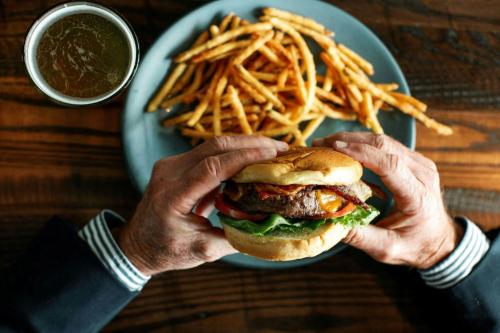 a man holding a hamburger and french fries on a plate at The Stella Hotel, Autograph Collection in Bryan