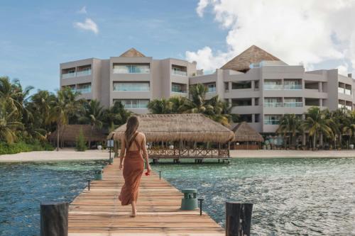 a woman walking down a dock in front of a resort at Almare, a Luxury Collection Resort, Isla Mujeres, Adult All-Inclusive in Isla Mujeres
