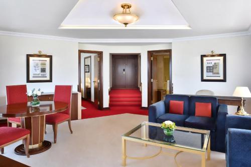 a living room with a blue couch and red chairs at Sheraton Grand Doha Resort & Convention Hotel in Doha