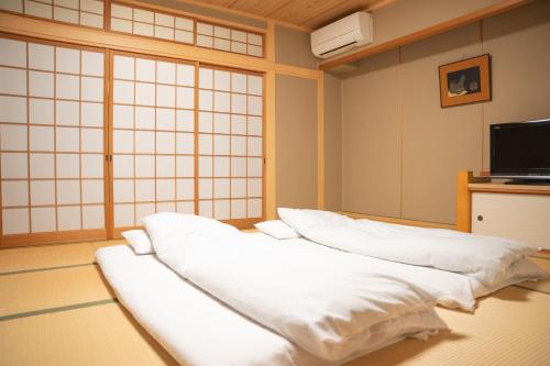 a room with white sheets on the floor and a tv at Yumoto Kanko Hotel Saikyo in Nagato