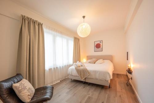 a bedroom with a bed and a chair and a window at kindvriendelijk appartement "Sereno", De Haan-Wenduine in Wenduine