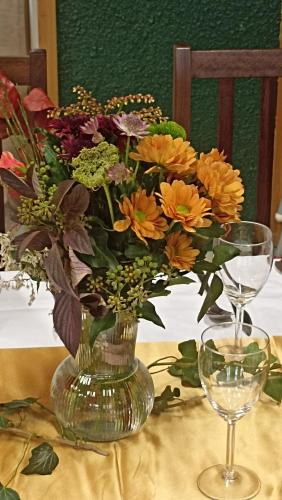 a vase of flowers on a table next to a wine glass at Penzion Slunečno in Dobšín