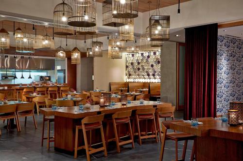 a restaurant with wooden tables and chairs and chandeliers at Renaissance Dallas at Plano Legacy West Hotel in Plano