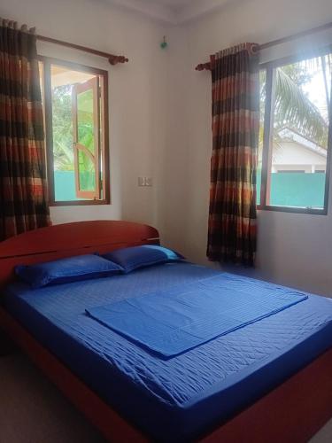 a bedroom with a bed with blue sheets and two windows at Guesthouse Dilush in Beruwala