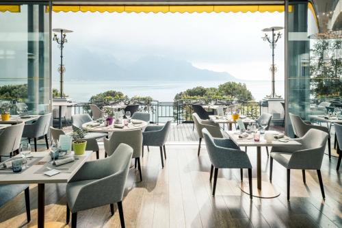 a restaurant with tables and chairs and a view of the ocean at Grand Hotel Suisse Majestic, Autograph Collection in Montreux