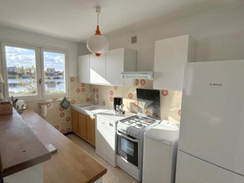 Il comprend une cuisine équipée d'appareils électroménagers blancs et d'un réfrigérateur blanc. dans l'établissement Maison individuelle familiale face à l'étang 6GLYC25, au Barcarès