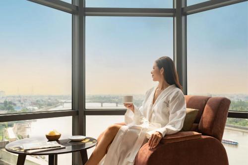 a woman sitting in a chair holding a cup of coffee at Sheraton Can Tho in Can Tho