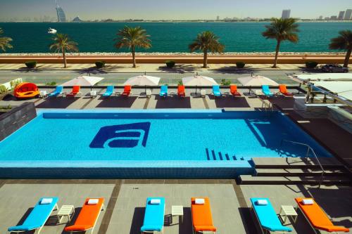 a swimming pool with chairs and umbrellas and the ocean at Aloft Palm Jumeirah in Dubai