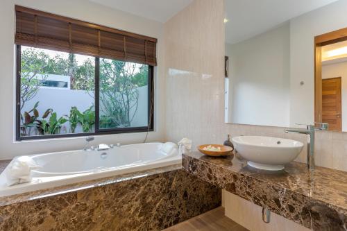 a bathroom with a tub and a large window at La Ville Phuket Pool Villa in Nai Yang Beach