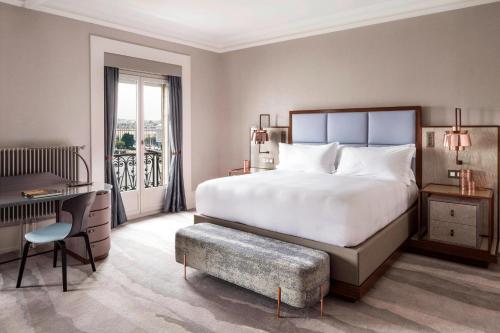 a bedroom with a large white bed and a desk and a window at The Ritz-Carlton Hotel de la Paix, Geneva in Geneva