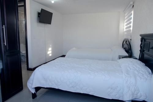 a bedroom with a white bed and a television at Hostería El Prado in Ibarra