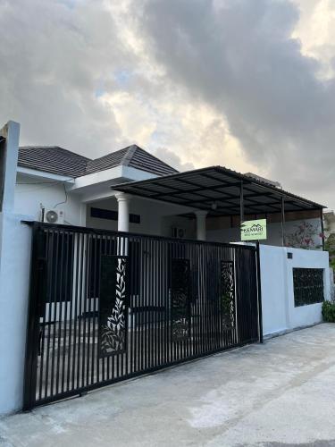 a white house with a black gate and a building at Kemari Homestay in Ulin