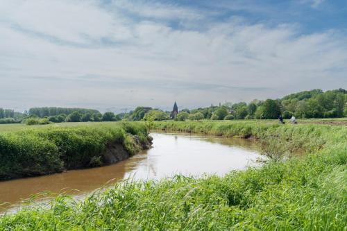 a river flowing through a field with a church in the distance at B&B de ZIL in Herselt
