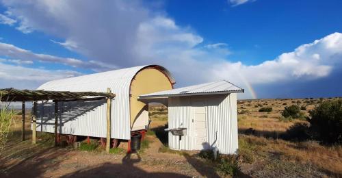 a white shed in a field with a rainbow in the sky at Dopper Joris Bruidswa Adam se Uitspanning in Orania