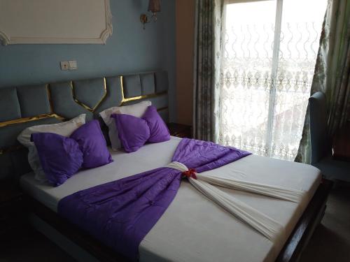 a bed with purple and white pillows and a window at Menat Hôtel in Yaoundé
