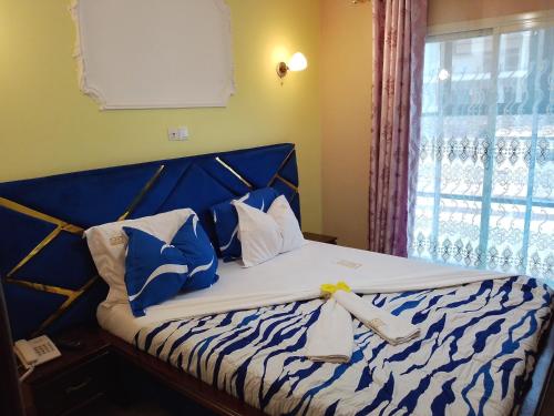 a bed with blue and white pillows and a window at Menat Hôtel in Yaoundé