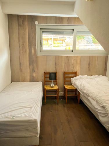 deux lits dans une chambre avec deux chaises et une fenêtre dans l'établissement Charmant duplex à Font-Romeu Odeillo Via, à Font-Romeu-Odeillo-Via