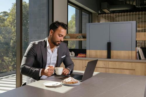 a man sitting at a table with a cup of coffee and a laptop at Courtyard by Marriott Perth Murdoch in Fremantle
