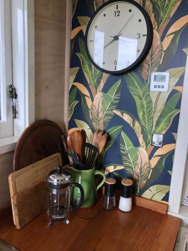 a clock on a wall above a wooden table at Raglan LoveNest -Romantic escape with outdoor bath in Raglan