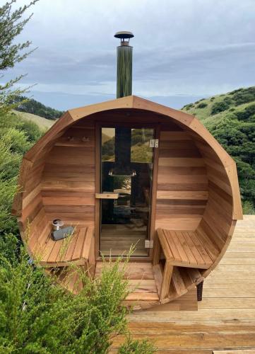a wooden sauna with a glass door on a wooden deck at Raglan LoveNest -Romantic escape with outdoor bath in Raglan