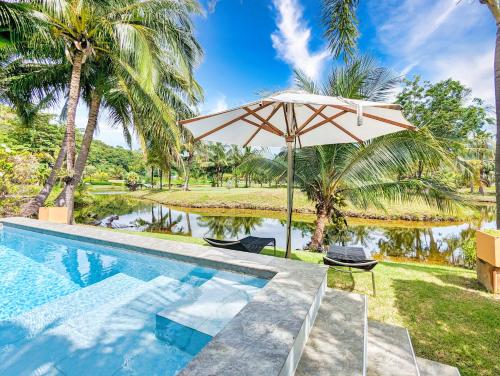 Una sombrilla y sillas junto a una piscina. en Poolside Villa - by KohChangVillas, en Ban Khlong Son