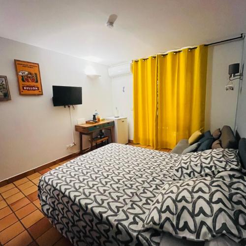 a bedroom with a bed and a desk and yellow curtains at Studio La "KAZ À COCO" Tartane in La Trinité