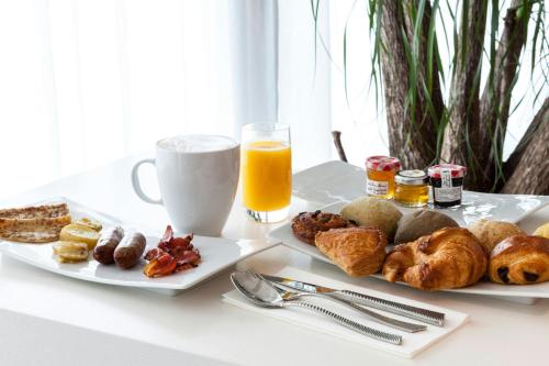 a table with two plates of breakfast foods and a glass of orange juice at AC Hotel by Marriott Paris Le Bourget Airport in Le Bourget