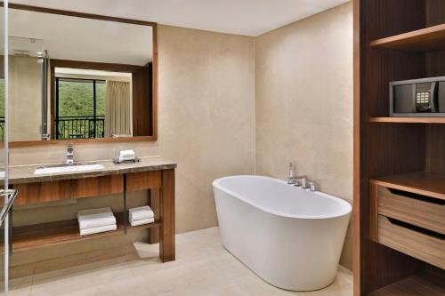 a bathroom with a tub and a sink and a mirror at Courtyard by Marriott Mahabaleshwar in Mahabaleshwar