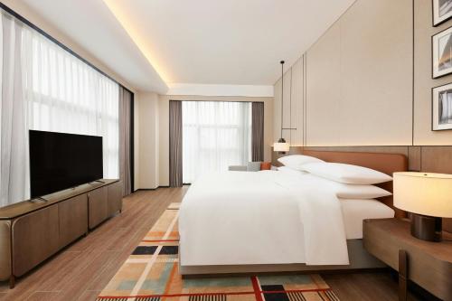 a bedroom with a large white bed and a flat screen tv at Courtyard by Marriott Nanning Wuxiang in Nanning