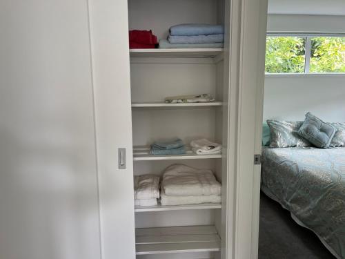 a closet with towels and a bed in a room at Guacamole Cottage in Tauranga