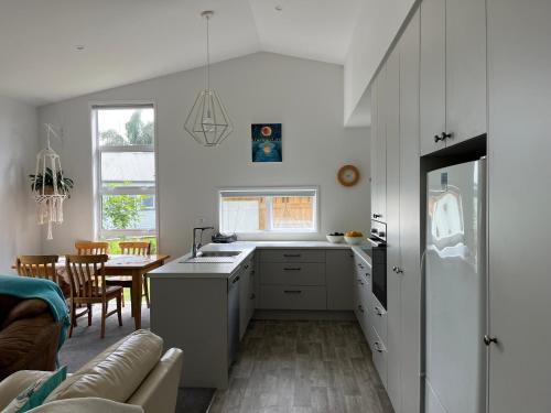 a kitchen with white cabinets and a table with a couch at Guacamole Cottage in Tauranga