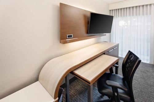 a desk in a room with a tv and chairs at Courtyard by Marriott Fort Lauderdale North/Cypress Creek in Fort Lauderdale