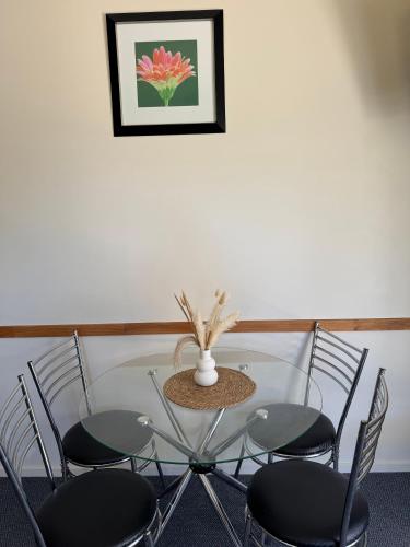 a glass table with four chairs and a vase on it at Bay Road Motels in Haast