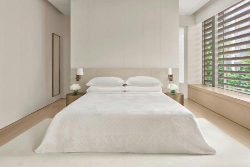 a white bedroom with a white bed with two tables at The Singapore EDITION in Singapore