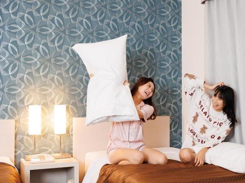 two girls laying on a bed holding a pillow at J Hotel Rinku in Tokoname